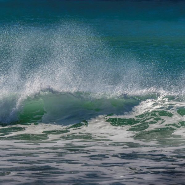 pexels-photo-7962163-7962163 Close-up view of a crashing ocean wave with spraying foam and vibrant blue water.